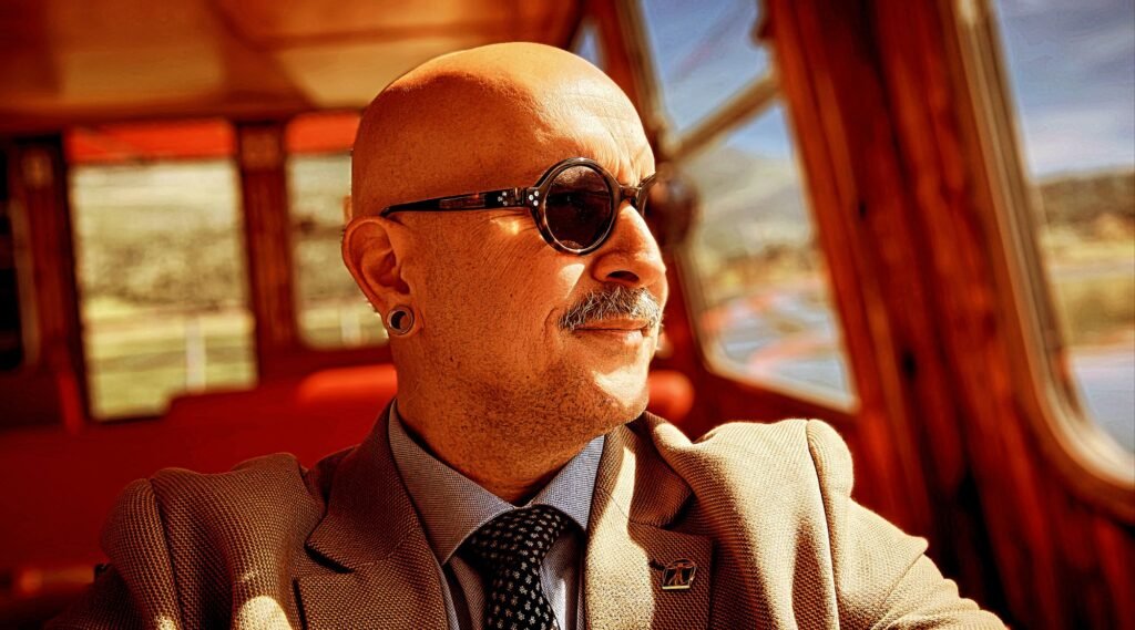 Portrait of artist Konstantinos Papamichalopoulos wearing round sunglasses and a suit in warm sunlight.